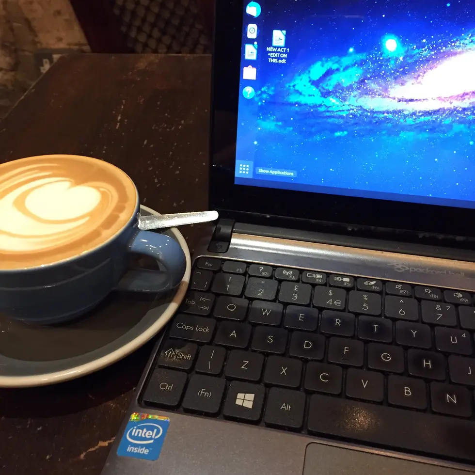 Writing in a cafe: picture of laptop computer with a file called New Act 1 on the desktop, and a fresh cup of coffee on the table
