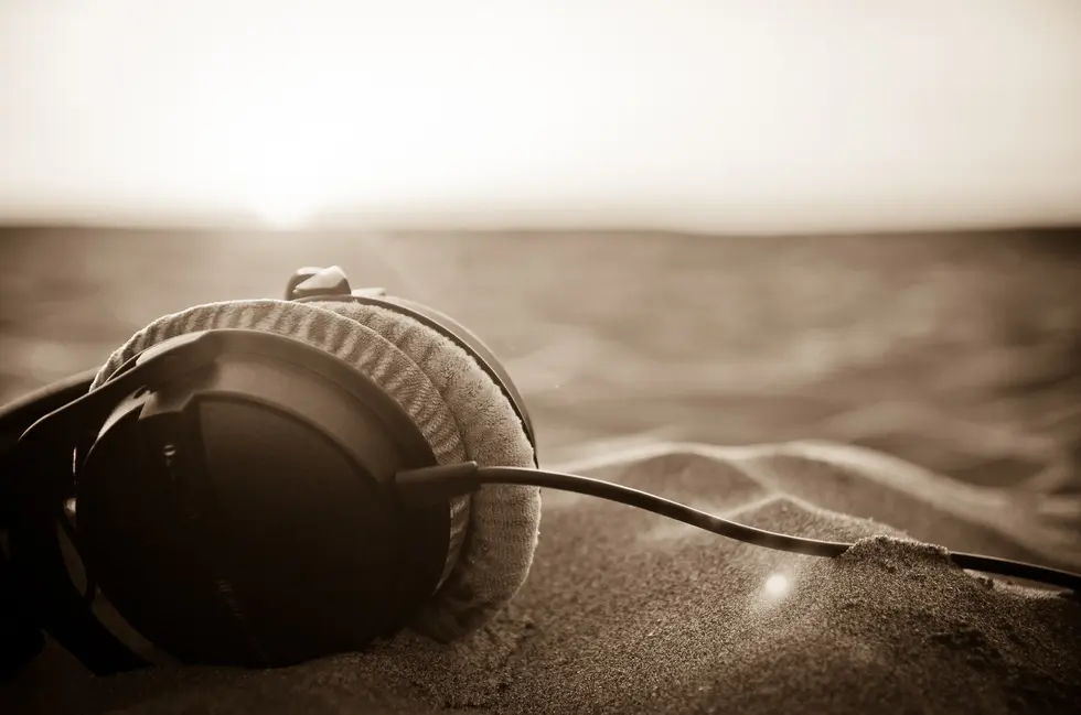 A pair of over-the-ear headphones lying in sand (Photo by Thibault Maestracci / Unsplash)